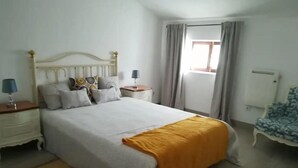 Une chambre à coucher avec un lit, des tables de chevet, une chaise et une fenêtre avec des rideaux.