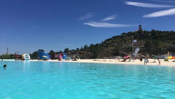 Une plage à l’eau turquoise et limpide, un rivage sablonneux et, au loin, une colline surmontée d’une tour.