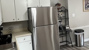 Una cocina moderna con armarios blancos, un refrigerador de acero inoxidable, una estantería de metal negro y un cubo de basura.