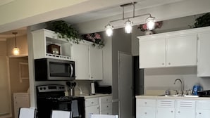 Una cocina moderna con armarios blancos, microondas, estufa y pileta. Hay un comedor con una mesa y sillas de madera.