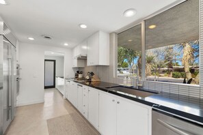 Une cuisine moderne avec des meubles blancs, un plan de travail noir et une grande fenêtre donnant sur l’extérieur.