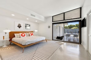 A modern bedroom with a large bed, a view of an outdoor patio, and a flat-screen TV mounted on the wall. - California Retro - 1963 Gem on 1/2 an Acre (Palm Desert)
