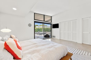 A modern bedroom with a large bed, a view of the outdoors, a TV, and a wardrobe. - California Retro - 1963 Gem on 1/2 an Acre (Palm Desert)