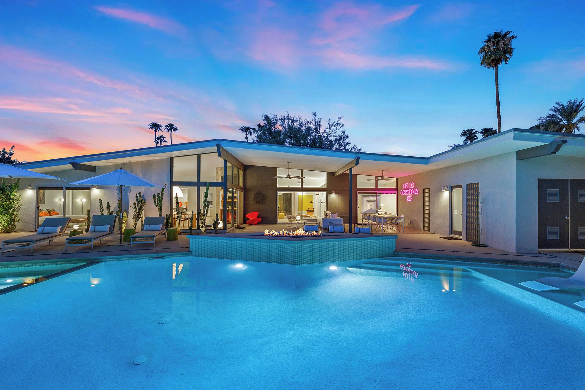 Una casa moderna con piscina, mobiliario exterior y un letrero de neón.