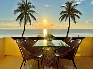 Relax in a serene outdoor seating area overlooking the calm sea, surrounded by wicker chairs and a potted plant.