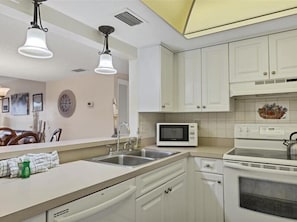 A kitchen with white cabinets, a microwave, a stove, a sink, and pendant lights.