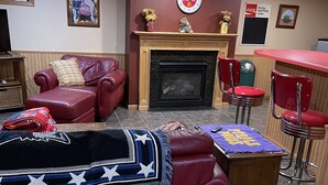 A living room with a fireplace, red leather sofa, wooden coffee table, and a red bar area. - Studio Apartment  (Willmar)