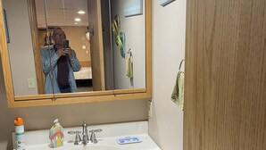 A bathroom with a wooden vanity, a large mirror, a sink, and a door with a handle. - Studio Apartment  (Willmar)