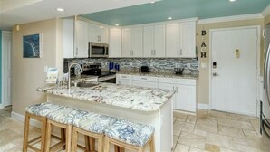 A kitchen with white cabinets, a granite countertop, a microwave, and a refrigerator.
