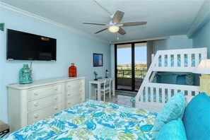 Une chambre à coucher comprenant un lit, une commode, un bureau, une télévision, un ventilateur de plafond et un balcon avec vue.