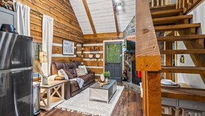 L’intérieur chaleureux d’un chalet, avec un revêtement mural en bois, une cheminée, un coin repas et un salon comprenant un canapé et une table basse.