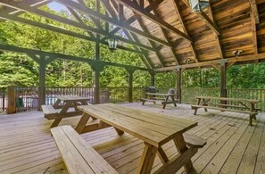 Un espace pique-nique abrité, doté de bancs et de tables en bois, entouré d’une clôture en bois et d’arbres.