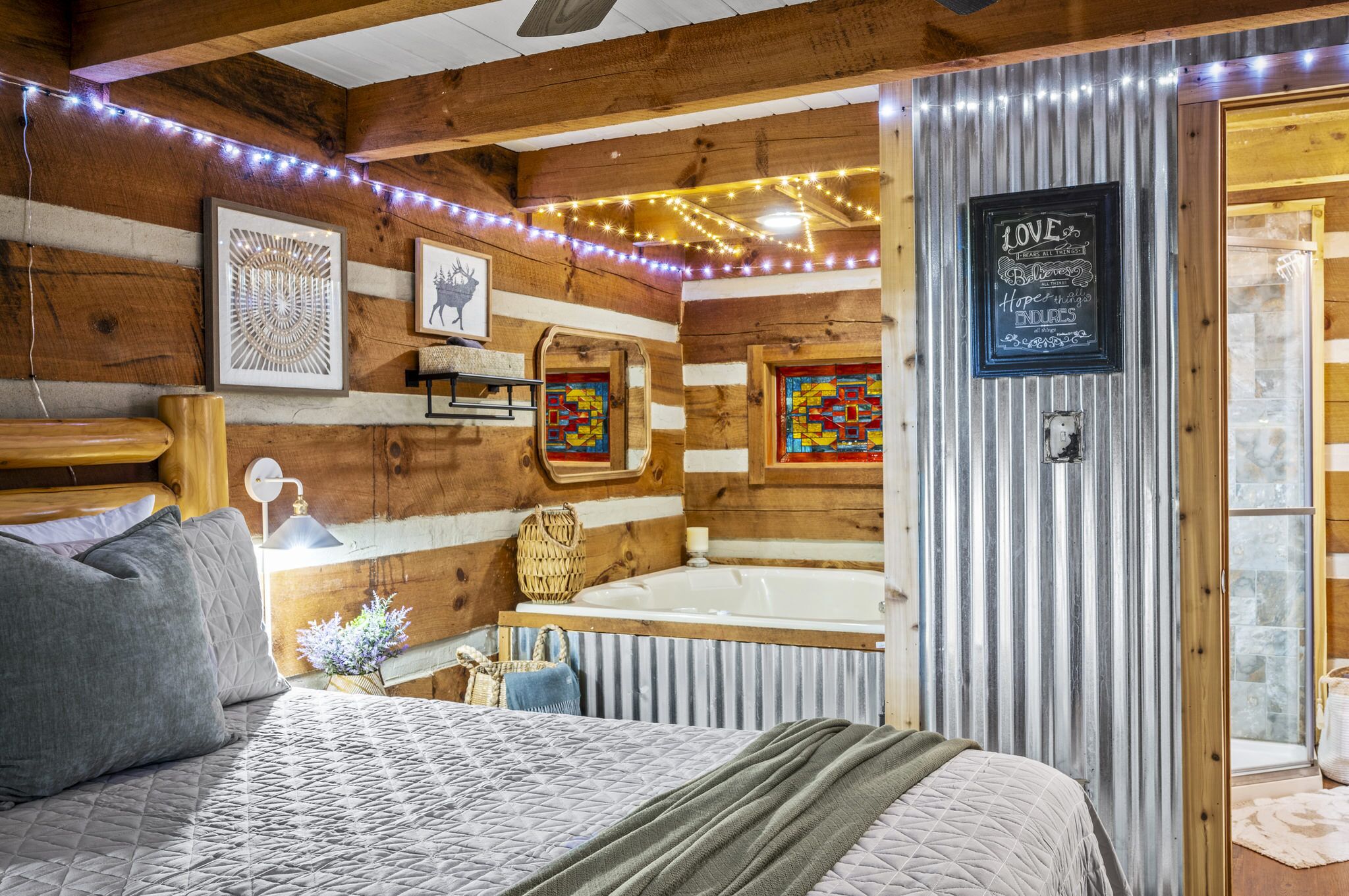 A cozy log cabin bedroom with a bed, a wooden headboard, a wall-mounted shelf, and a large window.