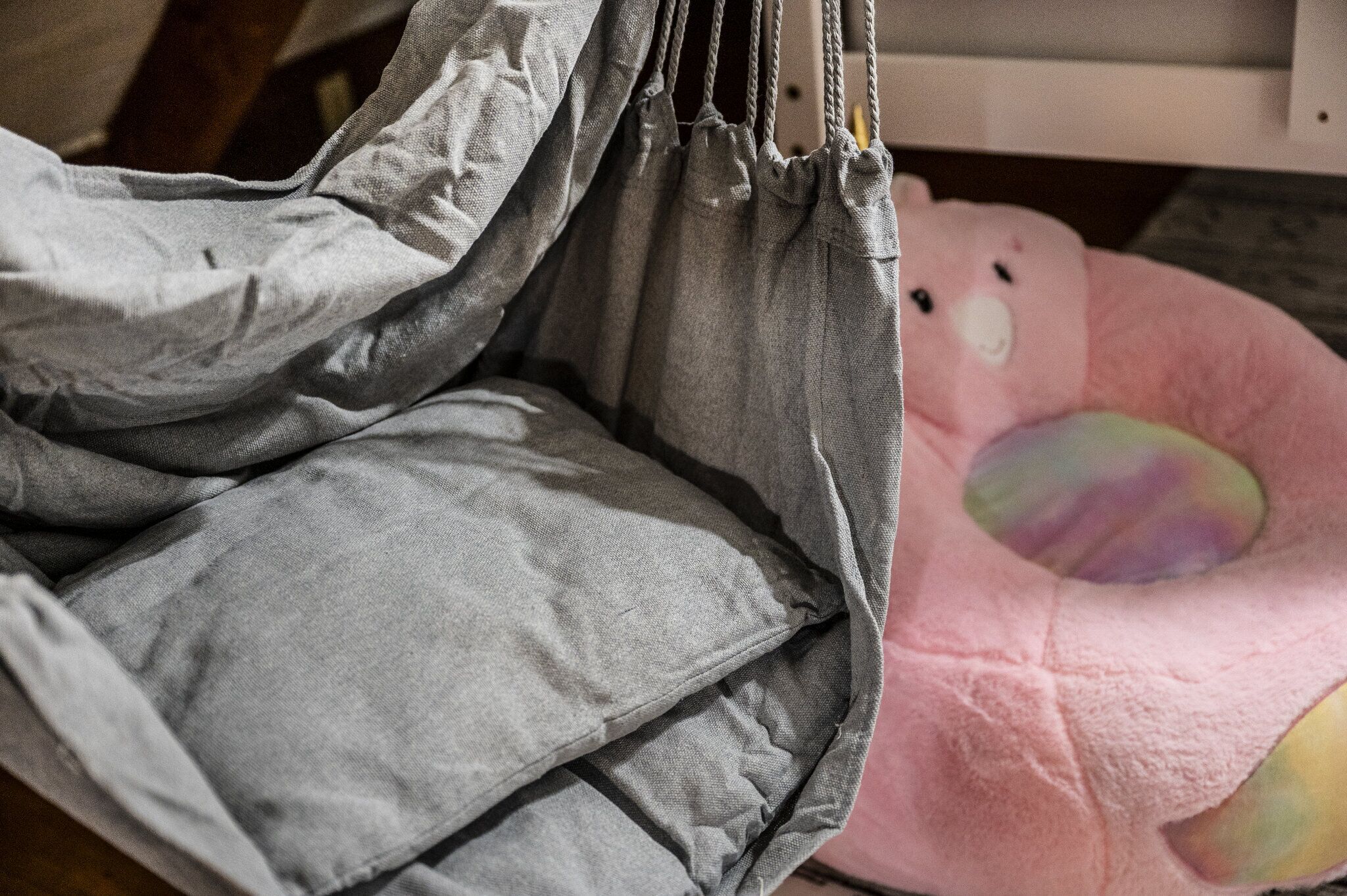 A grey fabric item with a drawstring, possibly a bag or a piece of clothing, and a pink plush toy with a rainbow-colored section.