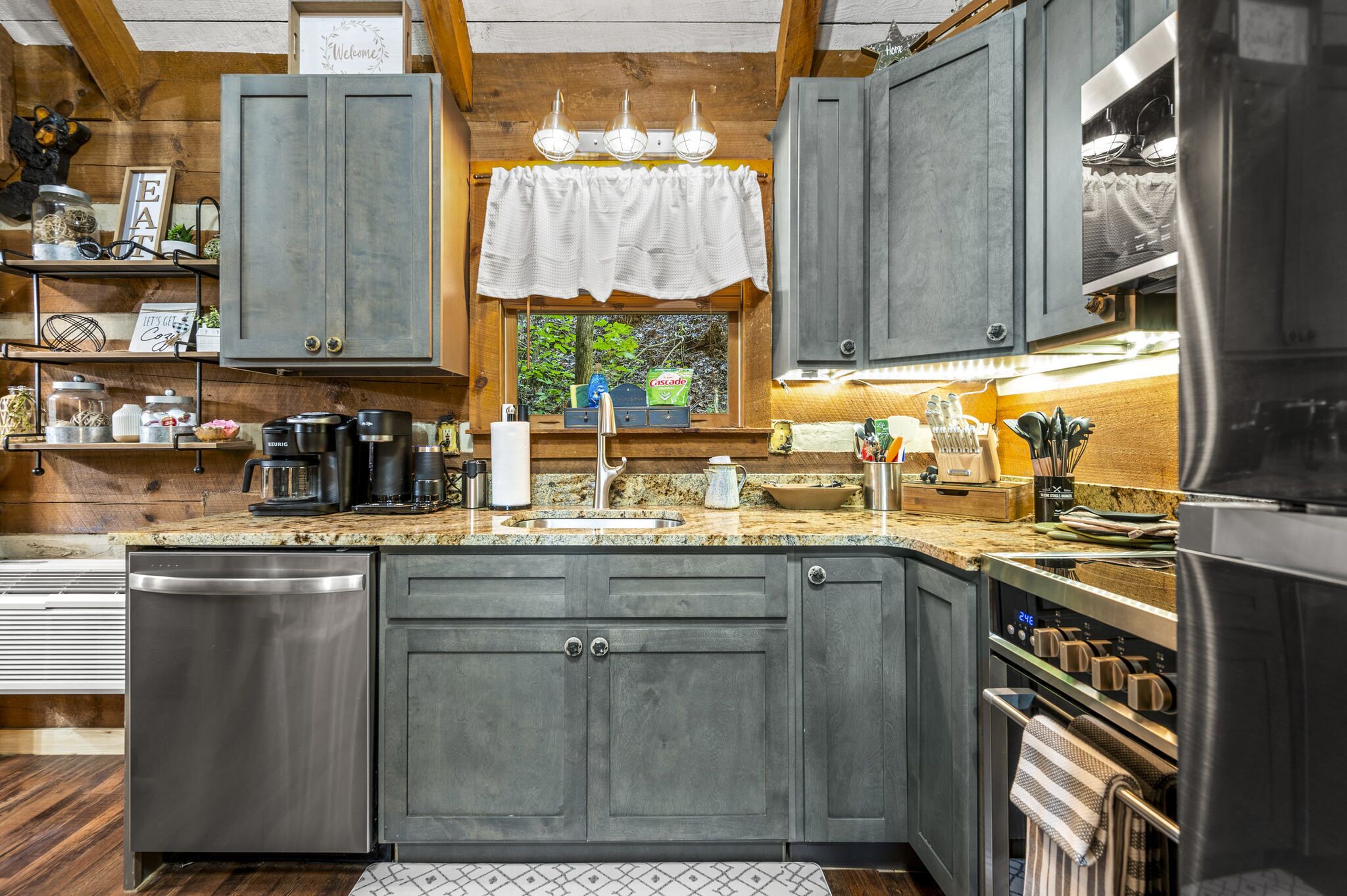 Une cuisine moderne avec des meubles gris, un plan de travail en granit, un four encastré et une fenêtre donnant sur un paysage verdoyant.