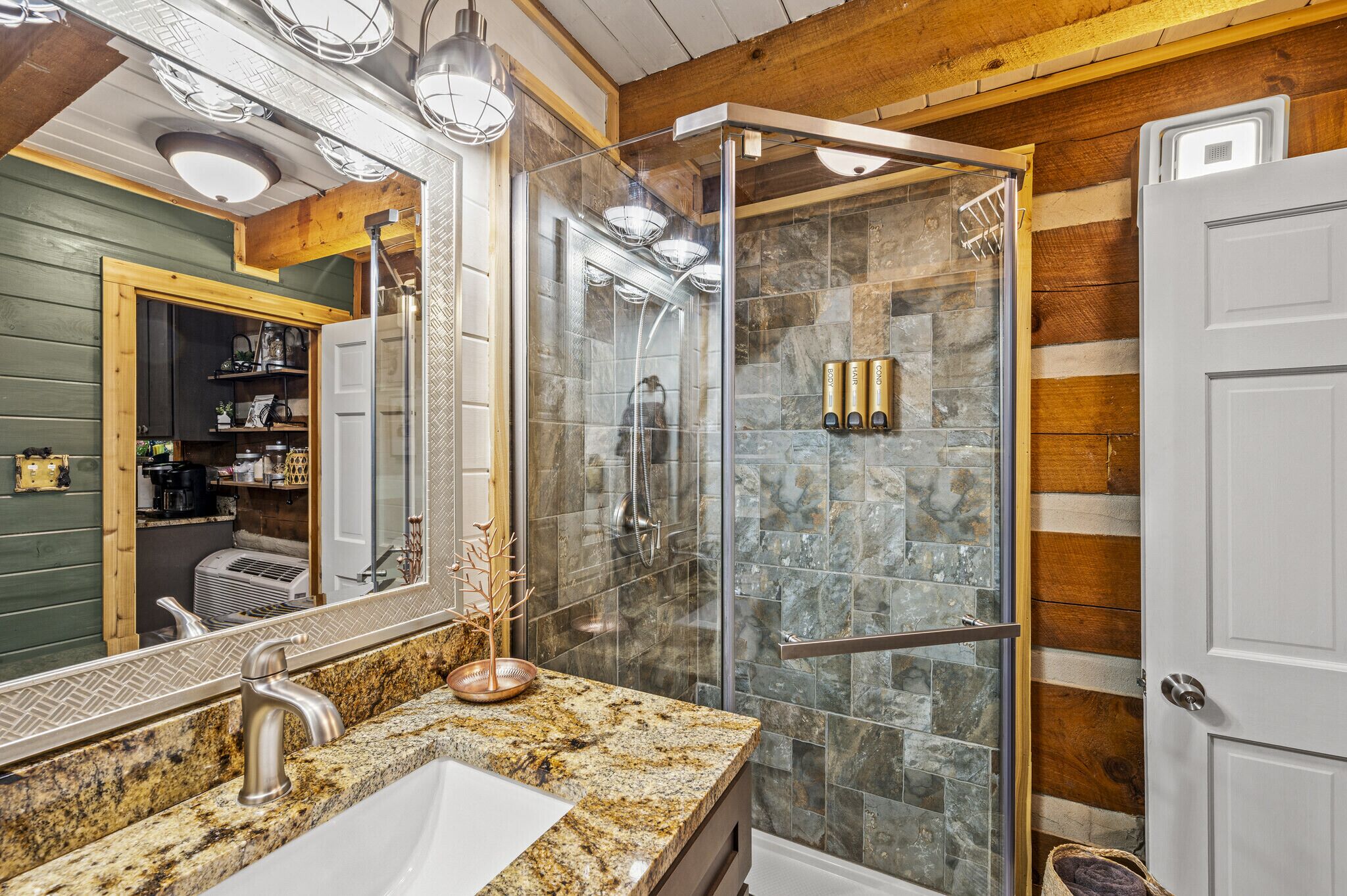 A modern bathroom with a granite countertop, a glass-enclosed shower, and a wooden ceiling.