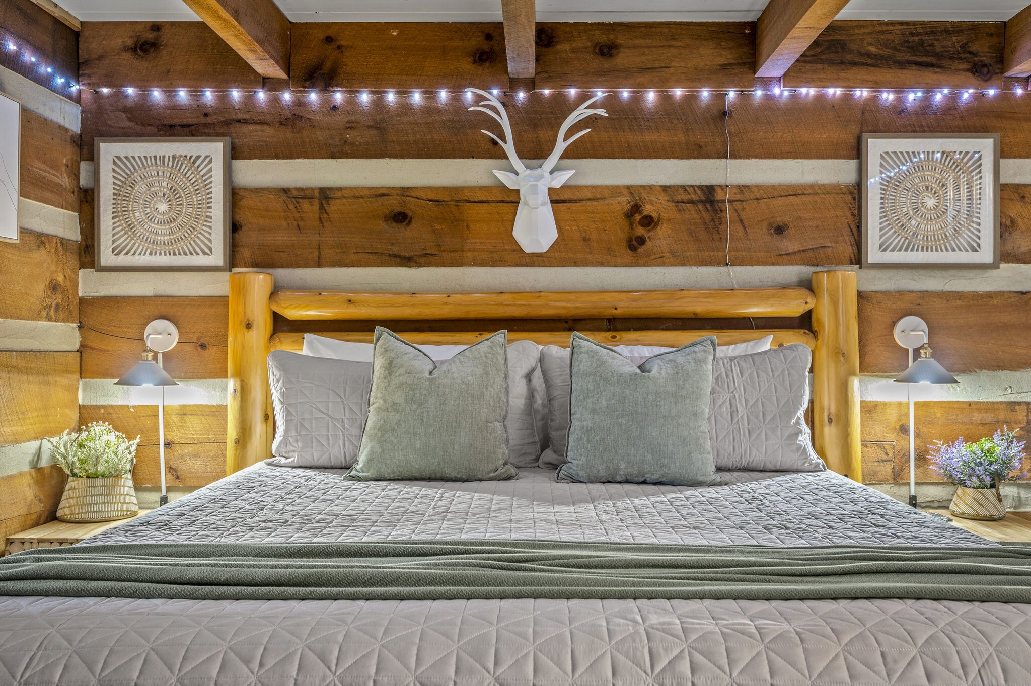 Un dormitorio tipo cabaña de madera con una cama, arte decorativo en la pared y una cabeza de venado montada.
