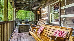 Une terrasse en bois avec une balançoire, une table avec des chaises et un espace barbecue.