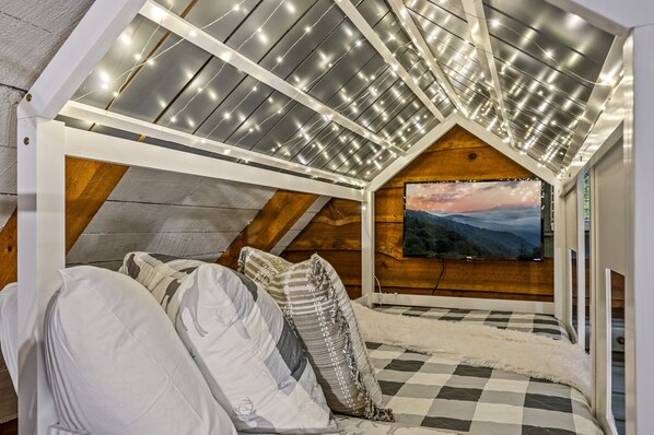 Une chambre mansardée chaleureuse, avec un plafond en pente, un sol à carreaux et une grande fenêtre offrant une vue panoramique.