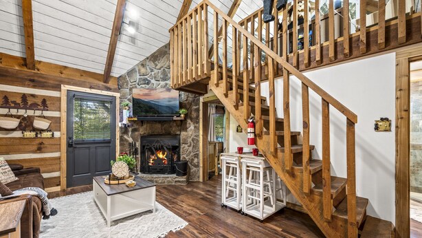 Un intérieur de chalet chaleureux avec une cheminée en pierre, un escalier en bois et un décor rustique.