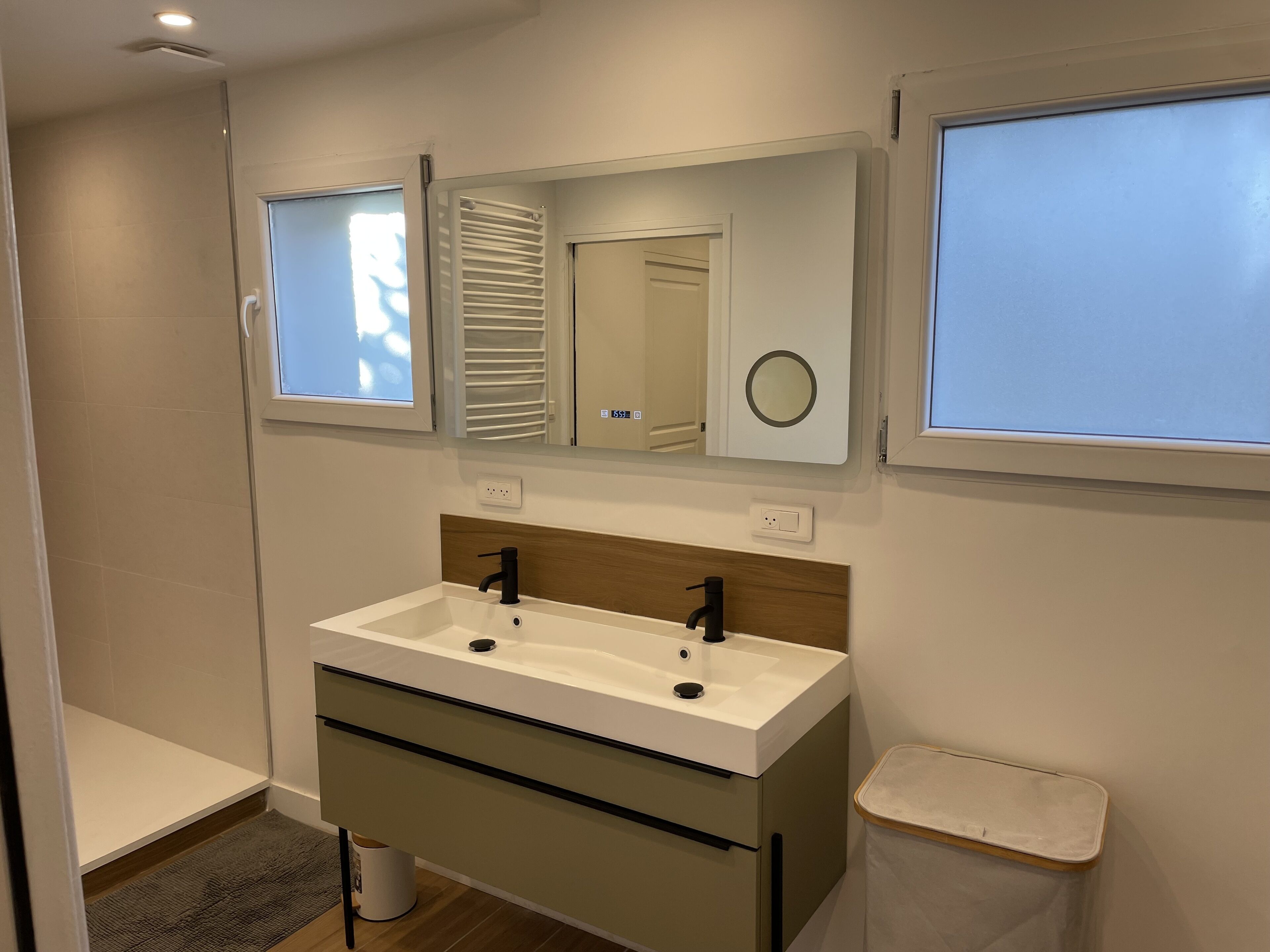 A modern bathroom with a white sink, wooden vanity, and a mirror above it.
