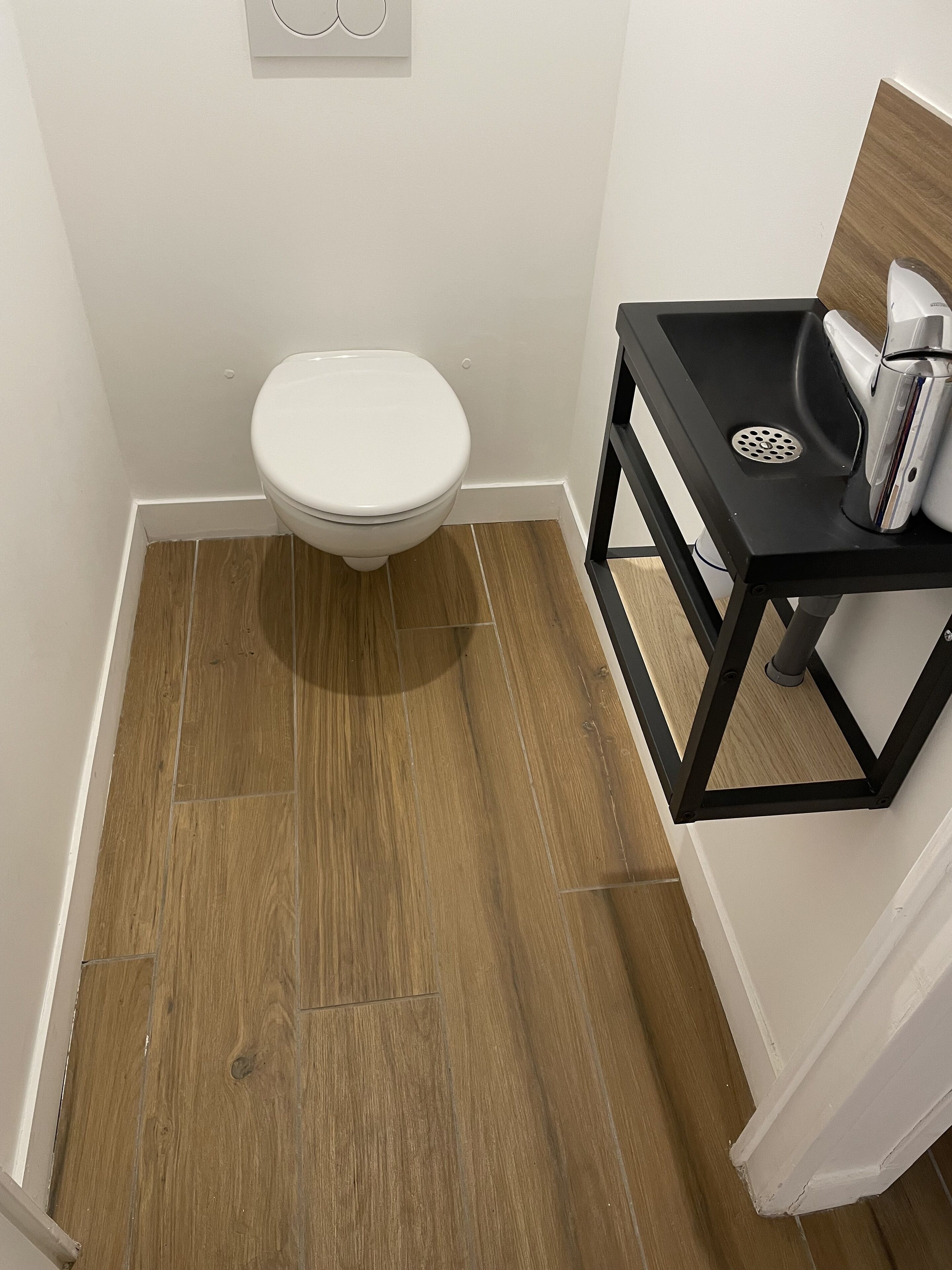 Ein kleines Badezimmer mit Toilette, Waschbecken und Spiegel sowie Holzboden.