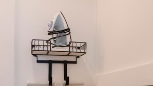 A wall-mounted ironing board with an iron, a towel, and a black metal shelf. - Historic Garden Studio, Steps from Pulaski Square⎮On-Site Parking (Savannah)