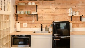 A compact kitchen with a wooden wall, a black refrigerator, a microwave, and a hanging pendant light. - Historic Garden Studio, Steps from Pulaski Square⎮On-Site Parking (Savannah)