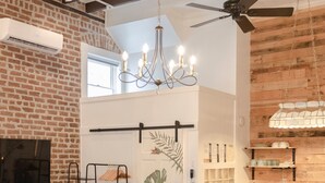 A bedroom with a bed, a wooden bench, a chandelier, a ceiling fan, and a brick wall. - Historic Garden Studio, Steps from Pulaski Square⎮On-Site Parking (Savannah)