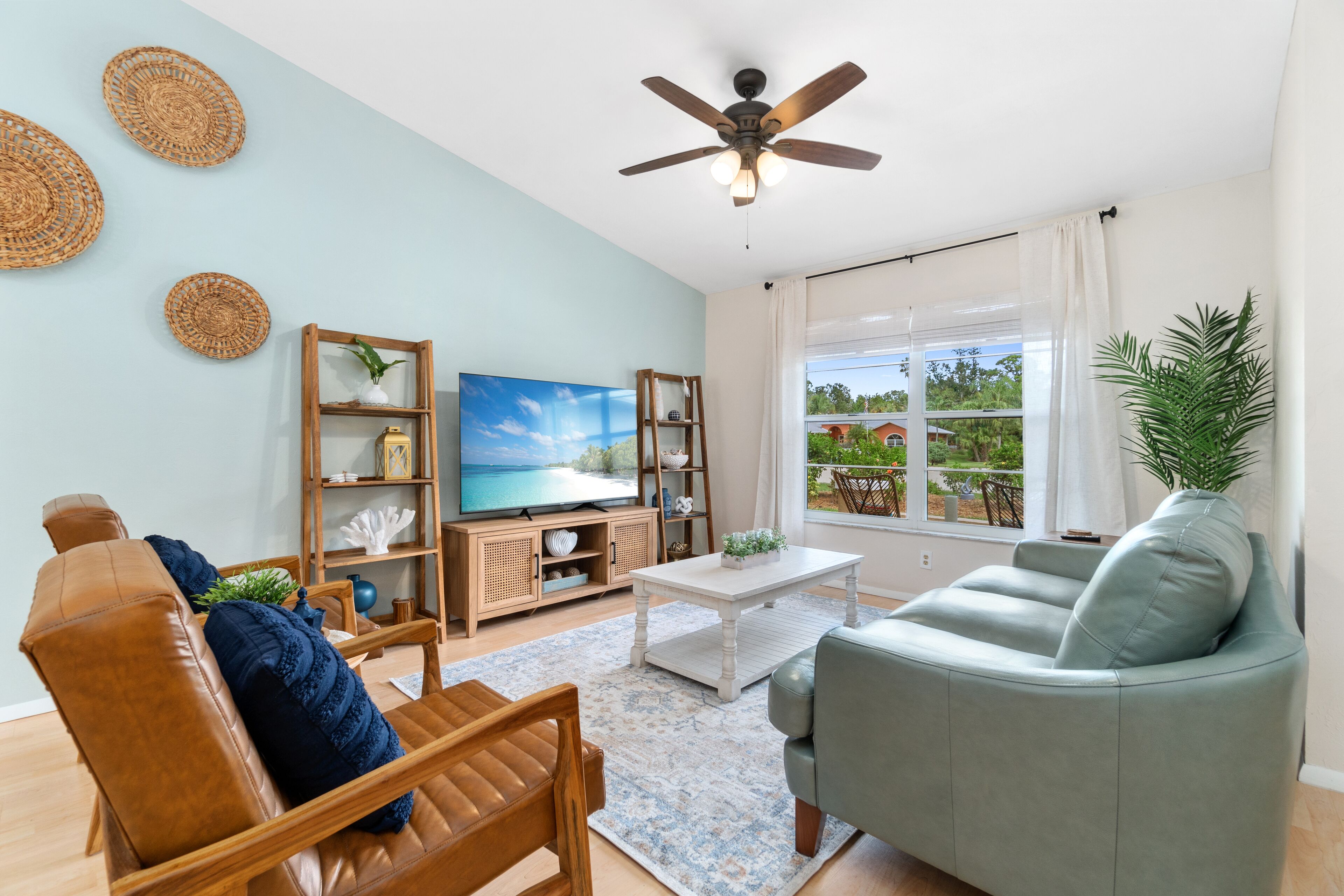 Una sala de estar con sofá, sillón, televisor, mueble de madera y ventilador de techo.