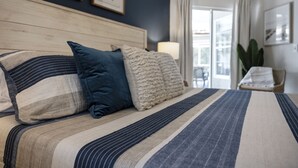Una cama bien hecha con ropa de cama a rayas y dos almohadas, un cabecero de madera y vistas a un balcón a través de una ventana.