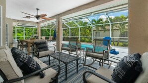 Un patio iluminado por el sol con piscina, mobiliario exterior y un ventilador de techo.