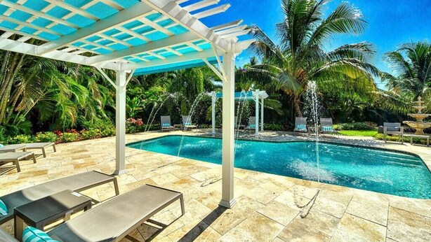 Ein Poolbereich mit einer Pergola, Liegestühlen und Palmen.