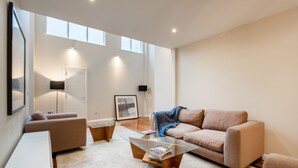 Una sala de estar moderna con una mesa de centro de vidrio, sofá color beige y un escritorio blanco.