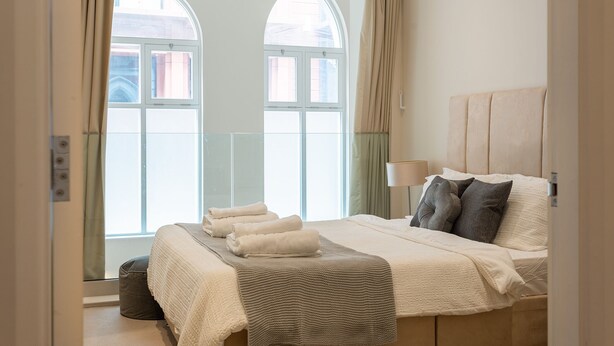Un dormitorio con una cama grande, una mesita de noche y una ventana con cortinas.
