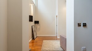 Un pasillo con suelo de madera, un cuadro enmarcado en la pared, una lámpara y un termostato también en la pared.