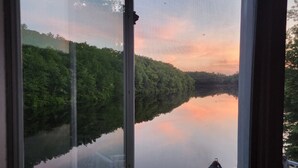 A view through a window of a lakeside property with a barbecue setup and outdoor seating. - SECLUDED WATERFRONT HOME WITH ROOM FOR ALL (Hopkinton)