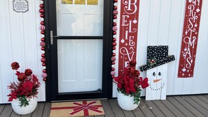 Puerta principal con marco negro, un cartel de bienvenida y adornos navideños, incluyendo un banderín, adornos y un recorte de un muñeco de nieve.