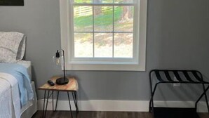 Un dormitorio con cama, mesita de noche con lámpara, ventana con persianas y una silla.