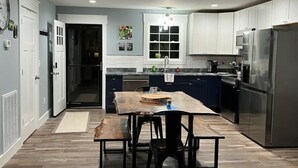 Una cocina moderna con armarios blancos, un refrigerador de acero inoxidable y una mesa de comedor de madera con sillas.