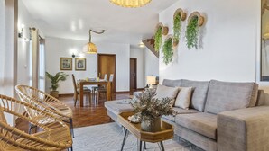 A living room with a sofa, wicker chairs, a wooden coffee table, and a dining area with a table and chairs. - Green Valley by Homie (Porto Moniz)