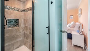 A bathroom with a shower, a glass door, and a tiled wall with a mosaic design.
