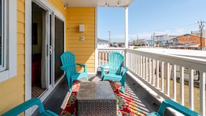 A balcony with turquoise chairs, a wicker table, and a colorful rug. - Dolphin Kisses @ Beach Harbor Condos. "B Bldg" - New in 2024. Linens Included! (Carolina Beach)