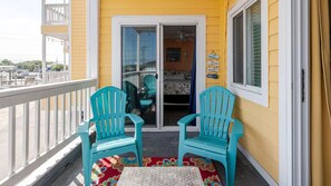 A balcony with two turquoise chairs, a small table, and a colorful rug.