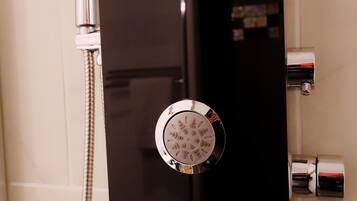 Eine Dusche mit drei runden, chromfarbenen Armaturen und einer Handbrause.