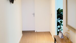 Um corredor com piso de madeira, porta branca, balcão de recepção com espelho e objetos decorativos fixados na parede.