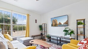 A modern living room with a large window, a sofa, a coffee table, and a TV mounted on the wall.