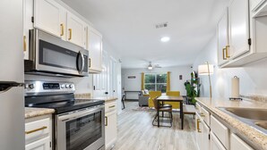 A modern kitchen with stainless steel appliances, white cabinetry, and a dining area with a yellow chair and table.