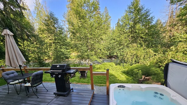 Terraza con jacuzzi, parrilla y zona de estar exterior con vistas a un área boscosa.
