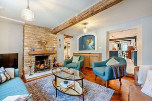 A living room with a stone fireplace, a glass coffee table, and two blue armchairs.